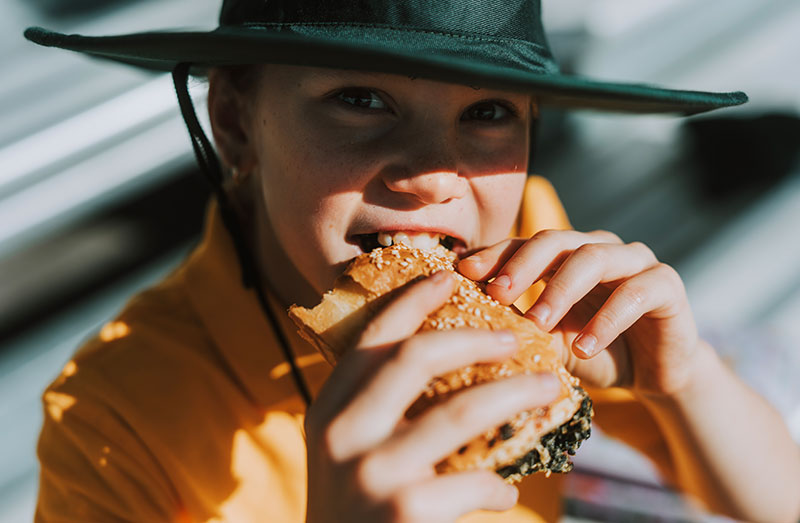 A girl in a school hat eats a bread roll.