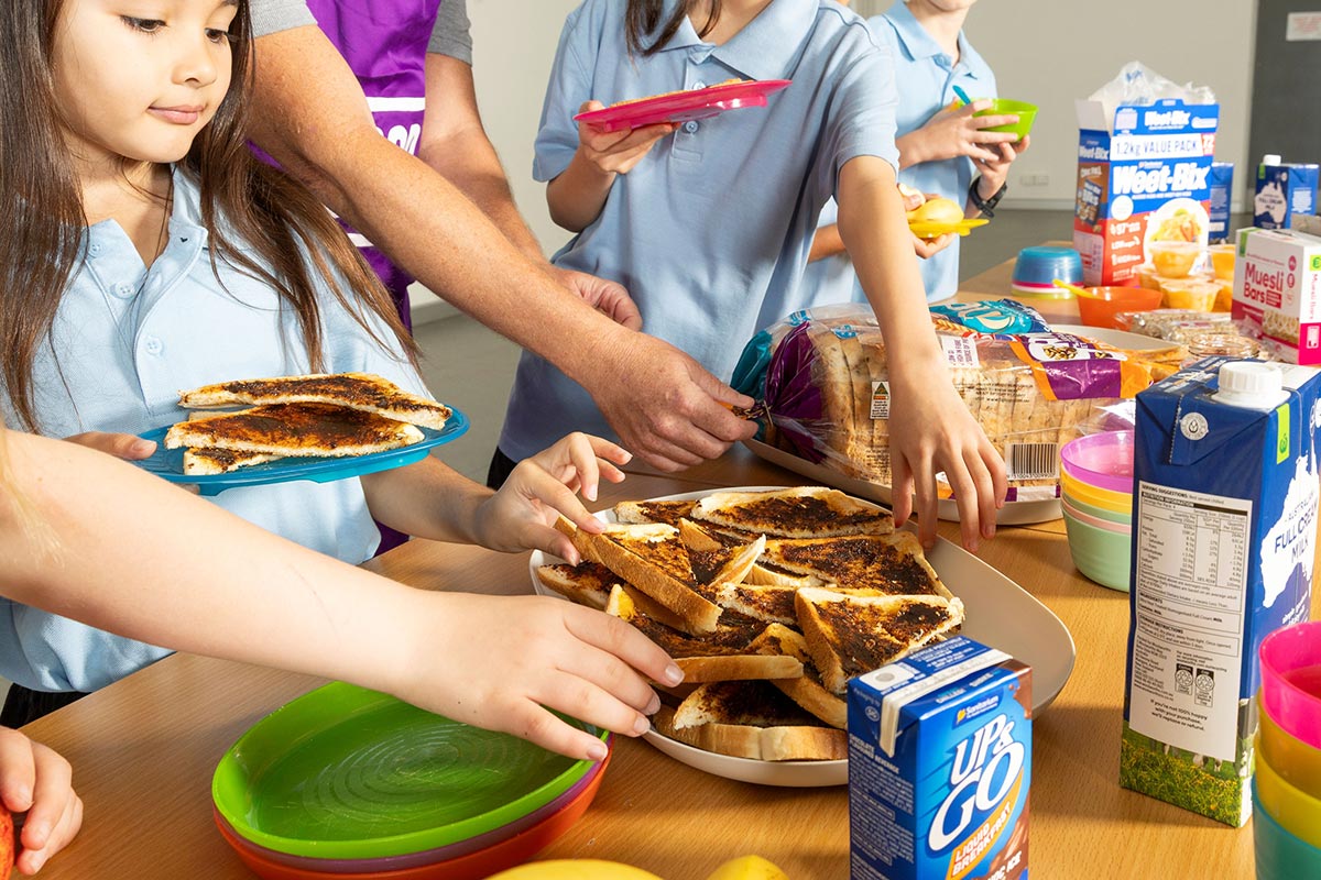 Children in school uniforms help themselves to toast, milk and cereal at a school breakfast.
