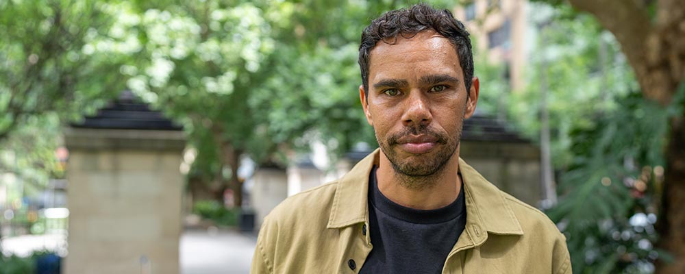 A man stands in a leafy city park, looking at the camera.